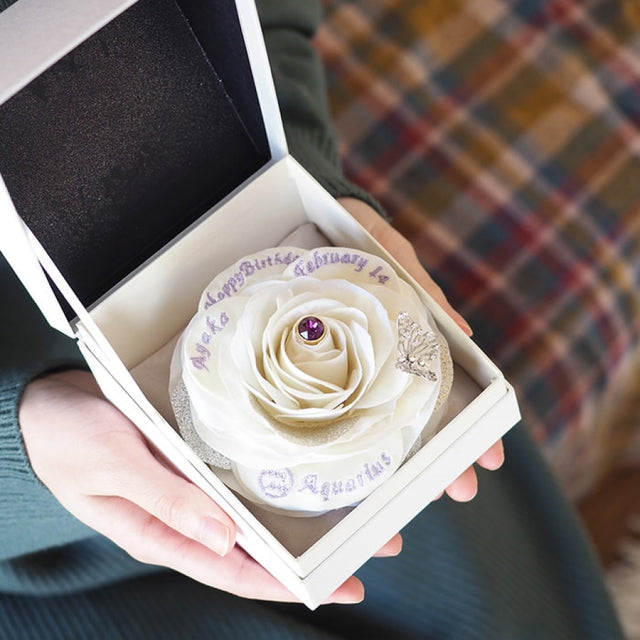 誕生石と名前・星座・誕生日の刺繍が入った、枯れない白い一輪バラを大切に持つ彼女。世界にひとつだけのオーダーメイドフラワーギフト。