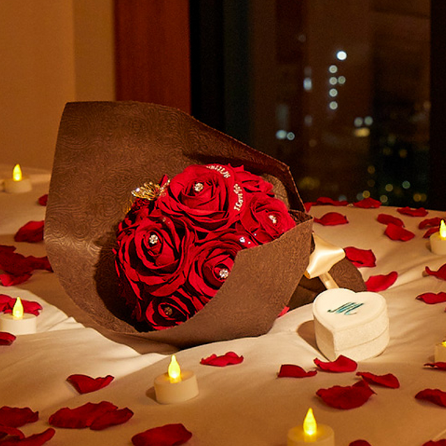12本の赤バラの花束が、花びらとキャンドルライトのサプライズ演出でベッドにセットされている。