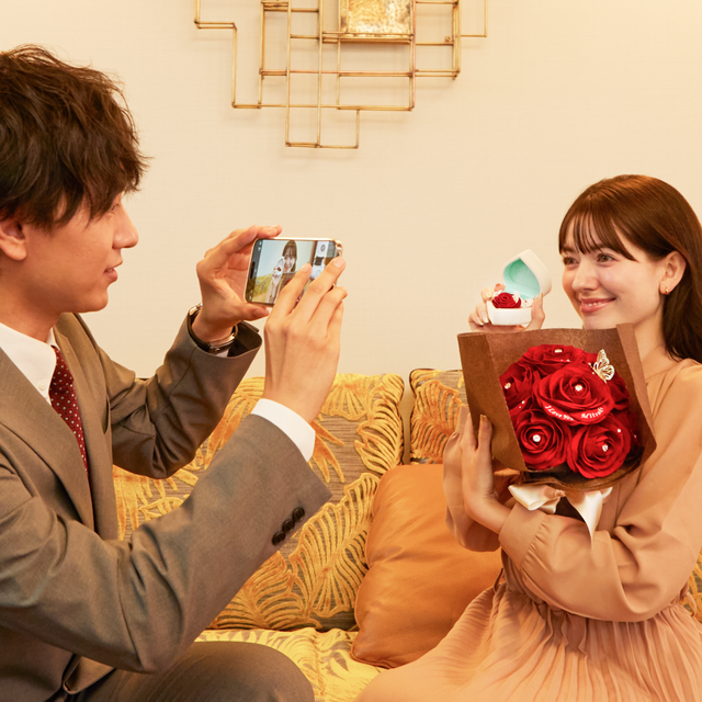 プロポーズを成功させた後、幸せそうな彼女の写真を撮る彼。赤いバラの花束は、キラキラと輝く装飾が施されているので、SNS映えする。