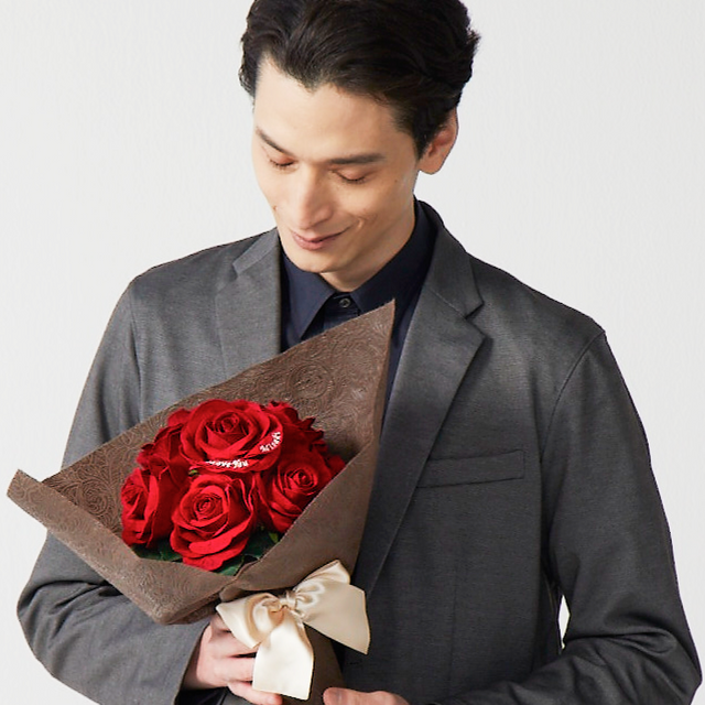 12本の大輪の赤いバラの花束を抱えた男性。12本の赤いバラはダズンローズと呼ばれ、バラ1本ずつに愛を意味が込められているので、プロポーズに人気。