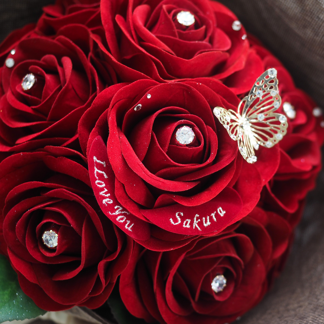 枯れることのないアートフラワー製の、12本の赤いバラの花束。花びらには、メッセージと名前が刺繍できる、特別なギフト。バラには輝くストーン装飾が施されていて、高級感がある。