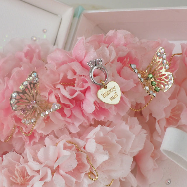 桜のアーチに囲まれたフェイクの指輪と「Marry me?」の蝶チャームが輝く、プロポーズ専用のラブブック。ピンクとホワイトのサクラで彩られた最終ページが、感動の瞬間を演出する特別なフラワーギフト。