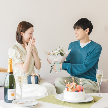 彼から差し出されたホワイトダズンフラワーに、驚きと喜びを隠せない彼女。リラックスした部屋でのサプライズプロポーズが、ふたりだけの特別な記念日に。