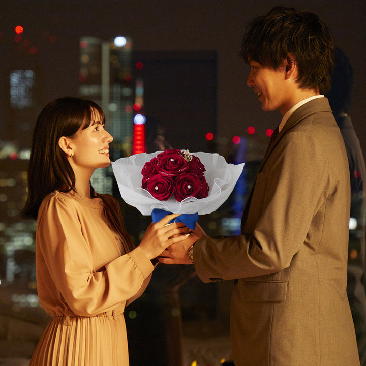 夜景の見える特別な場所で、赤いバラの花束を手渡しながらプロポーズをしている男性。プロポーズ場所として、夜景やホテルはロマンチックで人気。