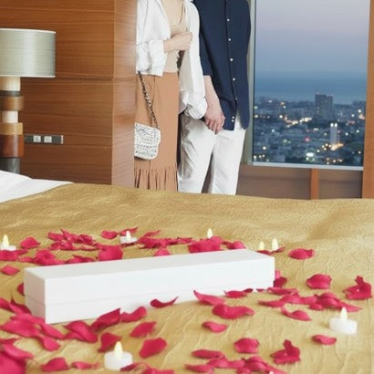 家やホテルなど、室内プロポーズならではの演出。赤いバラの花びら(造花)とキャンドル型LEDライトで、いつもとは違う特別な空間を演出する彼と、喜ぶ彼女のカップル。